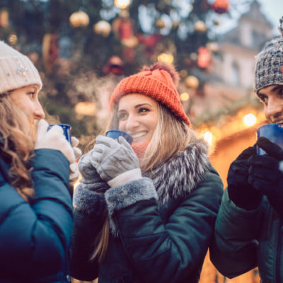Weihnachtsmarkt Pforzheim. Drei junge Frauen und ein Mann stehen in der Gruppe auf dem Weihnachtsmarkt und trinken ein Heißgetränk.
