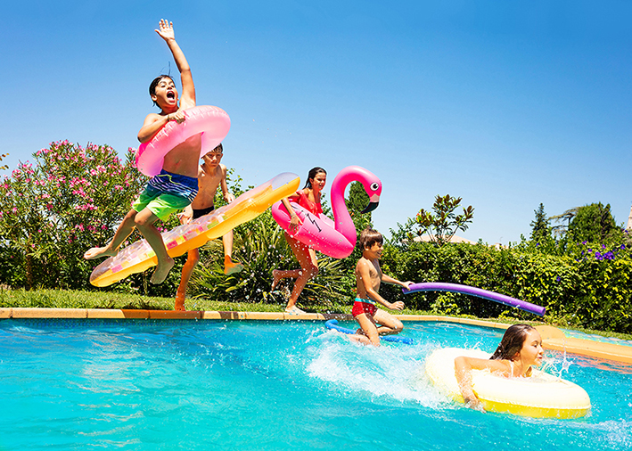 Kinder springen mit Schwimmreifen in ein Wasserbecken im Freibad