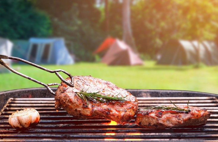Holzkohlegrill, mit dem verschwommenen Hintergrund eines Campingplatzes in einer Naturlandschaft.