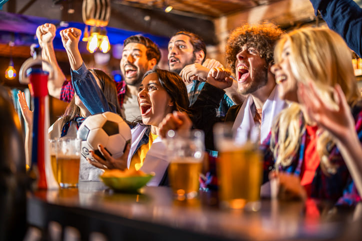 Eine aufgeregte Freundesgruppe hält den Fußball und feuert das Tor im Pub an.