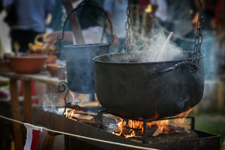Großer Eisenkessel oder Kessel mit dampfendem Eintopf über dem Feuer, Essen für alle auf einem Mittelalter Markt.