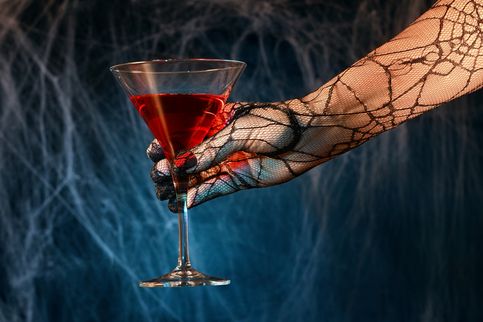 Behandschuhte weibliche Hand mit rotem Cocktail.