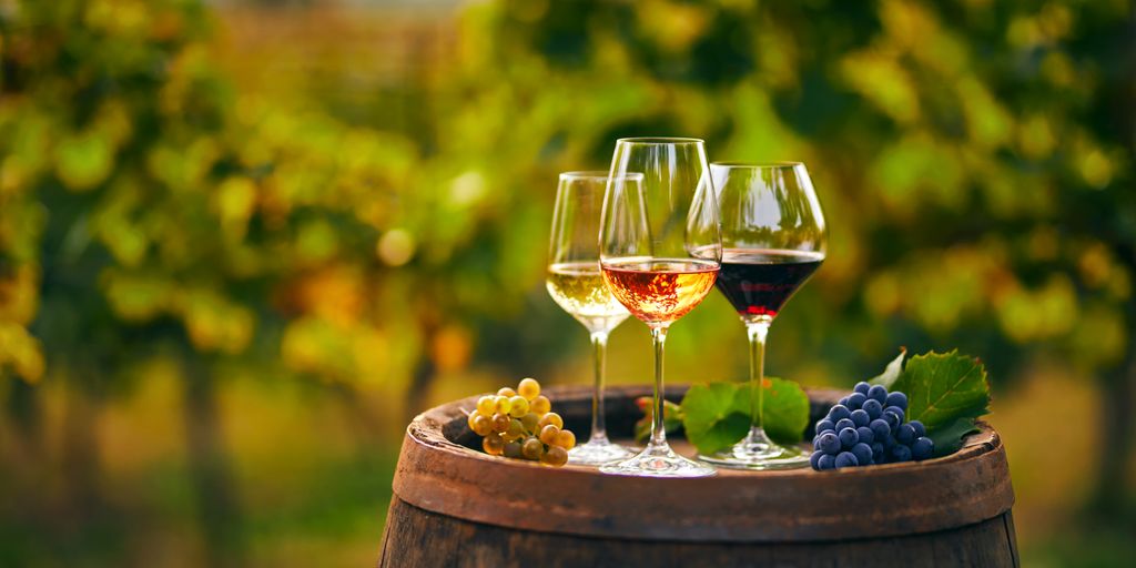 Drei Gläser mit unterschiedlichen Weinen und Trauben, auf einem Weinfass.
